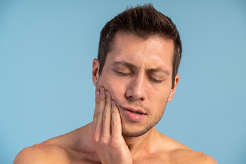 Obraz premium Young handsome man standing over isolated blue background touching mouth with hand with painful expression because of toothache or dental illness on teeth