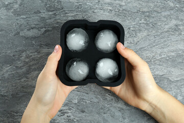 Woman holding mold with frozen ice balls at grey table, top view