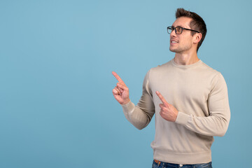 Advertise here. Positive bearded man pointing finger away paying your attention at empty space for advertisement. Indoor studio shot isolated on blue background