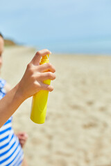Little girl in swimsuit hold in hand yellow bottle of sunscreen standing on the beach