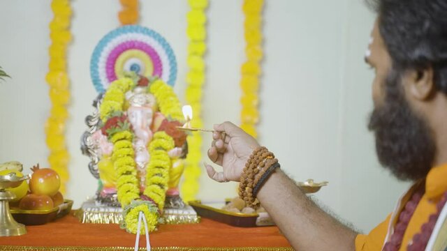 Focus on hand Holy god man or Indian priest offering aarti by chanting hymns in front of lord ganesh idol during festival celebration at home - concept of treditional festival and indian culture.