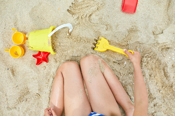 Top view of Little kid having fun on the beach and playing with sand toys