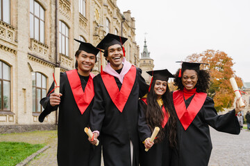Multiracial graduates wearing gown and caps making fun together