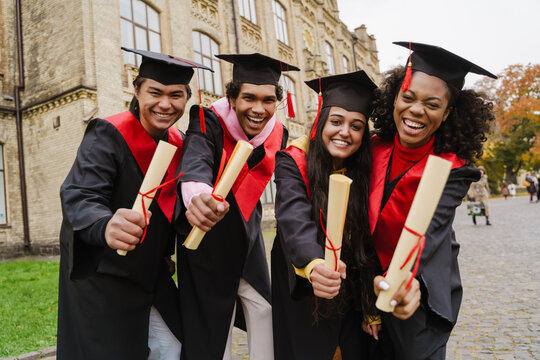 Multiracial graduates wearing gown and caps showing their diploma