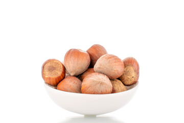 Several organic hazelnuts with a white ceramic saucer, close-up, isolated on white.