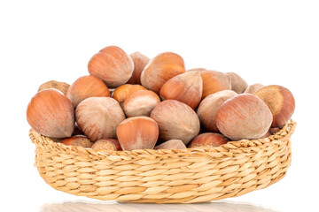 Several organic hazelnuts on a straw plate, close-up, isolated on white.