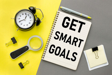 Get Smart Goals. Assorted yellow office stationery with magnifier and alarm clock on gray background. © Svetlana