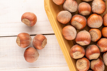 Several unpeeled hazelnuts with a tray of bamboo on a wooden table, close-up, top view.