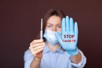 Coronavirus concept. Girl wearing mask for protection from disease and show stop hands gesture for stop corona virus outbreak. Stop the pandemic with vaccination. There is a syringe in the girl's hand