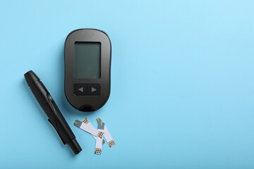 Digital glucometer, lancet pen and test strips on light blue background, flat lay with space for...