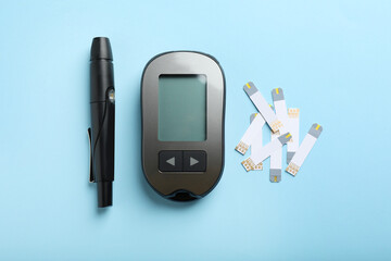 Digital glucometer, lancet pen and test strips on light blue background, flat lay. Diabetes control