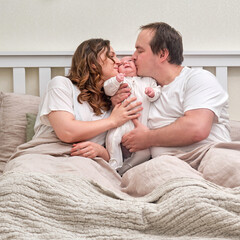 A man and a woman kiss a newborn baby on the bed. Father and mother of a child boy, happy parents and an infant baby in a home bedroom