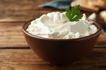 Bowl of tasty cream cheese and parsley on wooden table, closeup