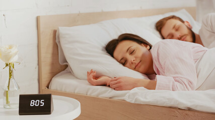 Brunette woman sleeping near husband and clock at home.