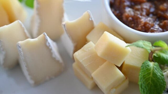 Different sorts of cheese in a plate with greens and sauce on black background.