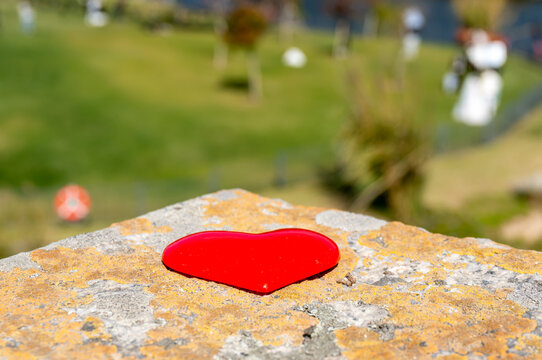 A red heart rests on a mottled stone in the sunlight, and in the distance newlyweds are having their wedding pictures taken. Valentine's Day theme, wedding scene.