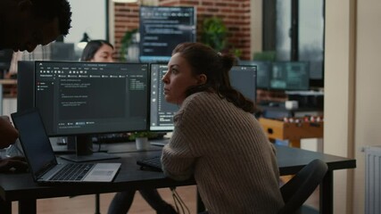 Junior developer putting laptop with source code on senior dev desk asking for opinion about database. Programer writing algorithm interrupted by colleague wanting help with fixing errors.
