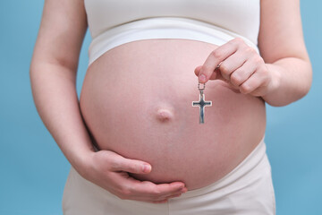 A symbol of the Christian religion in the hands of a pregnant woman, a studio photo on a blue background