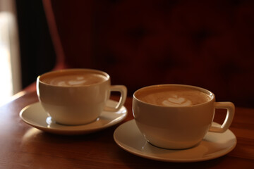Cups of aromatic coffee with foam on wooden table in cafe
