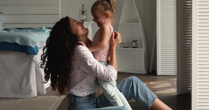 Little girl snuggle to her young mom. Loving Latin mum sit on floor in cozy bedroom hugs adorable daughter smile enjoy moment with eyes closed. Unconditional love, happy motherhood, adoption concept