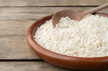 Narrow focus, raw carnaroli risotto rice in a plate over wooden table with copy space