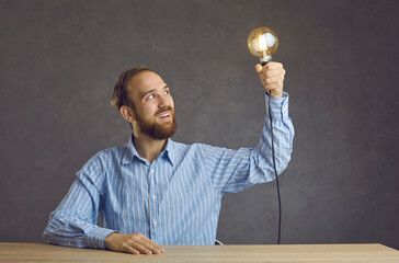 Portrait of excited man freelancer or entrepreneur holding glowing bulb in hand looking at light...
