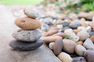 Rock stack on the stone courtyard with blur garden background on the sunshine day. Balance stones against the garden.