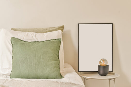 Cushions on comfortable bed near empty frame on nightstand table