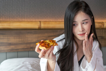 Happy young woman enjoy eating pizza on bed in hotel room. Beautiful female sitting in hotel bed eating pizza. Young woman hanging out eating pizza.