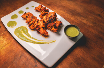 Barbeque spicy chicken in a white plate served with coriander dip sauce. Indian dip decorated for food presentation of an appetizer finger food.