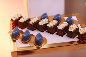 Candy bar on wedding party with a lot of different candies, cupcakes, souffle and cakes on golden plate.