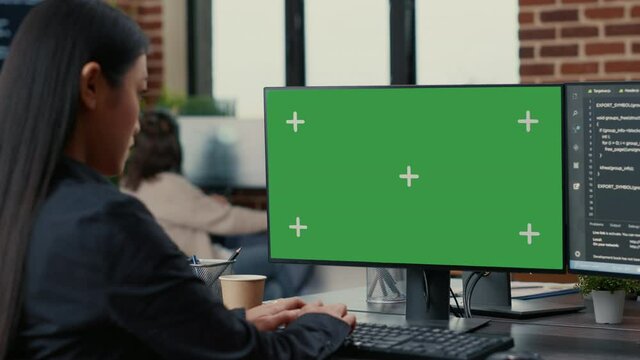 Focus on computer screen with green screen chroma key mockup in front of asian programer writing code in software development agency. Database coder programming sitting at desk.