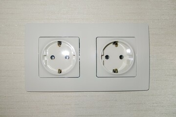 Double electrical outlet on the wall with wallpaper. The color is ivory.