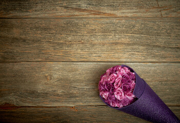 Light and dark purple roses in glittering violet paper on a wooden background. Text space. Celebrations, Valentine's Day, birthday party, wallpapers. Minimal style. Top view. Flat lay.