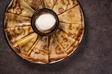 Stack of pancakes on a plate with sour cream. Traditional for the Russian pancake week. Dark background