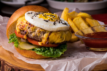 Hamburger. Sandwich with chicken burger, tomatoes, pickled cucumber and fried egg. Fresh tasty chicken burger on wooden table.