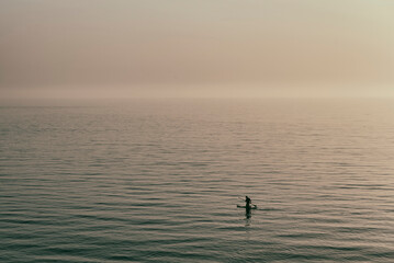 Fototapeta premium Silhouette of a man paddle boarding on the sea during sunset