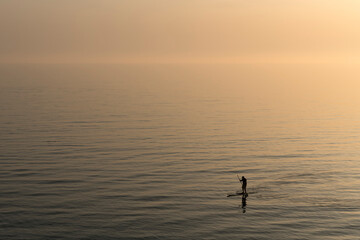 Man practicing stand up paddle boarding on the sea after sunset
