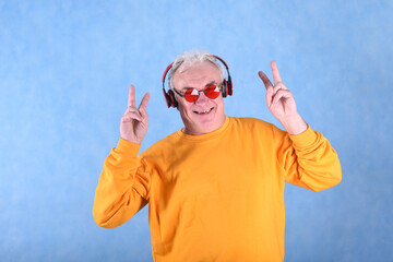 A man of retirement age gray-haired having fun with music in headphones in the studio on a blue...