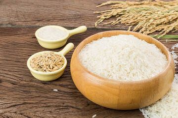 Organic white rice or jasmine rice in a wooden bowl with the ears of rice lying on the wooden floor