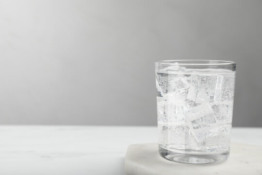 Glass of soda water with ice on white table. Space for text