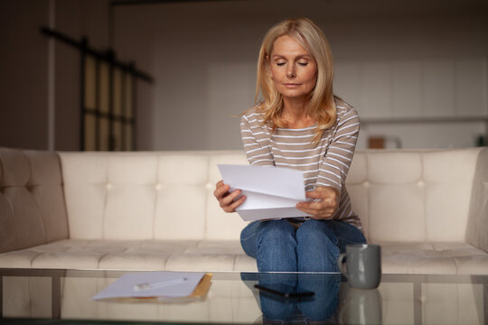 Postal advertising, promotion. Mature woman reads a letter at home. Corporate reply by mail.