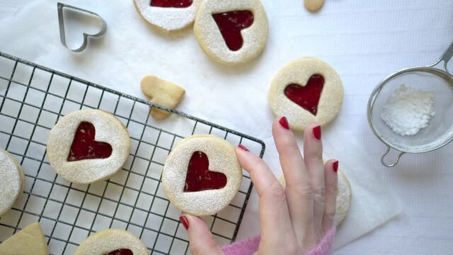 Top down view a person takes a bite from a Linzer Cookie. Heart shape raspberry jam filled biscuits. White background with modern and contemporary style. 4k real time motion. Romantic food concept