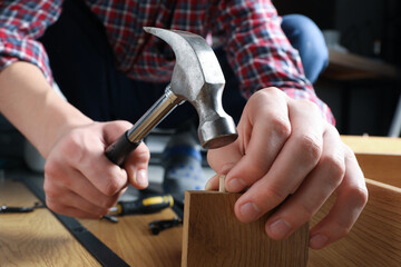 Man with hammer assembling wooden furniture indoors, closeup