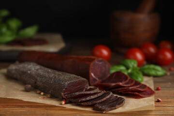Delicious dry-cured beef basturma with basil and tomatoes on wooden table, closeup