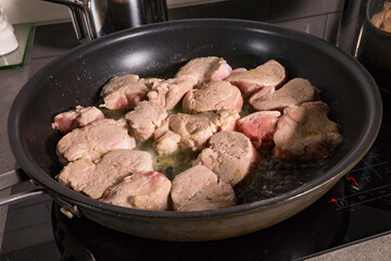 Pork tenderloin frying in a frying pan.