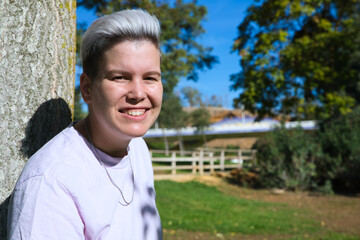 gender non-binary and androgynous person doing different postures and leaning on a tree. He is...