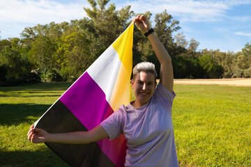 gender non-binary person is holding the flag of non-binary pride in his hands in the wind. He is...
