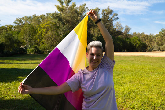 gender non-binary person is holding the flag of non-binary pride in his hands in the wind. He is looking at the camera. Concept of non-binary and androgynous. Diversity
