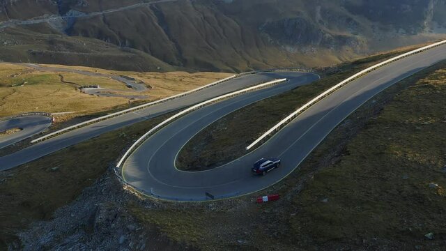 4K Aerial view of a blue SUV all terrain car driving on the amazing mountain road in Romania, Transalpina, during a summer sunrise. Winding road landscape.